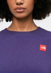Purple cotton crewneck sweatshirt with ribbed neckline, featuring a small red logo patch that reads "The North Face."