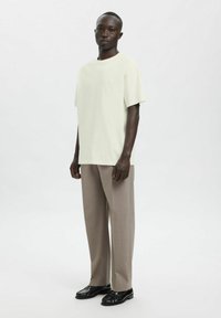 Kortærmet, lysegrøn t-shirt kombineret med lysebeige, vidde bukser og sorte sko. Minimalistisk design, glat tekstur og afslappet pasform.