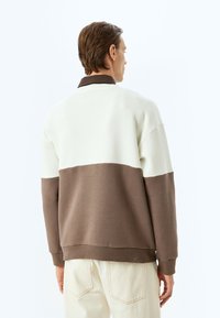 Sudadera con un diseño a bloques de color, en la parte superior color crema y en la parte inferior marrón oscuro, fabricada con material de algodón suave. Mangas largas y cuello.