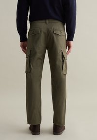 Olivgrüne Cargo-Hosen mit zwei Seitentaschen, geradem Schnitt und glatter Textur, getragen mit braunen Wildleder-Stiefeln.