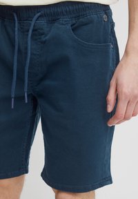 Pantalones cortos azul marino hechos de una tela suave, con cinturilla elástica con cordón, bolsillo lateral y detalles de costura simples.