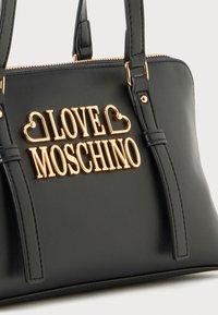 Črna usnjena torbica z zlatim logotipom "LOVE MOSCHINO", ki vsebuje srčkaste detajle, dve ročaji in zgornje zadrgo.
