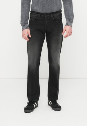 Jean en denim noir avec une coupe droite, décoloré sur les cuisses, cinq poches et une fermeture à boutons. Porté avec des baskets noires et un sweat gris.