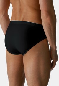 Gli slip da nuoto neri presentano una texture liscia, un design a vita bassa e una cintura elastica a contrasto. La vista posteriore mostra una copertura completa.