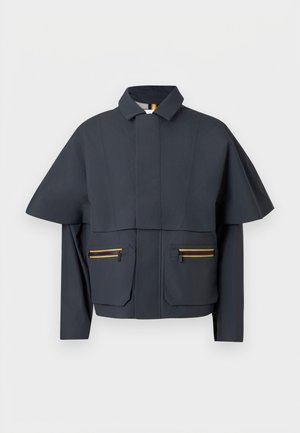 Veste courte pour homme en tissu bleu marine foncé ; manches surdimensionnées ; deux poches avant avec fermetures éclair orange ; col pointu ; texture lisse.