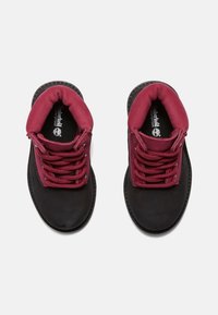 Botas de tobillo impermeables en negro y burdeos con un cuello acolchado, diseño de cordones y suelas texturizadas en contraste para mejorar el agarre.