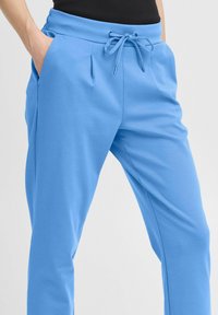 Blue sweatpants feature a drawstring waist, two side pockets, and a tapered fit with a lightweight, textured fabric.