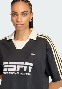 Μαύρο τζέρσεϊ από πολυεστέρα με λευκό λογότυπο "ESPN", κρεμ γιακά και τρεις κίτρινες ρίγες στον κάθε ώμο. Μικρό λογότυπο Adidas στο στήθος.