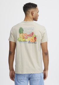 Beige bomulds T-shirt med et farverigt frugt grafik på ryggen, der har teksten "Florida's Finest" og "Shop local SUN CO. FRUIT."