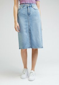 Světle modrá džínová midi sukně se rovným střihem, předními kapsami a knoflíkovým zapínáním. Stylizováno s bílými teniskami.