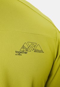 Dos d'une chemise en tissu vert clair perforé avec un logo de montagne contour noir et le texte « ensemble là-bas ».