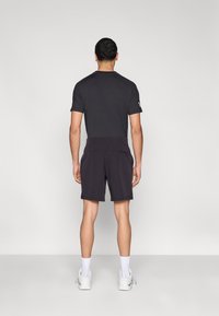 Črna športna majica in kratke hlače z oprijetim krojem in elastičnim pasom. Majica ima kratke rokave in vidno logotipno poudarjeno obliko.