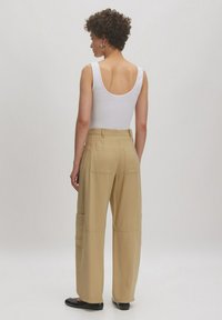 Tan wijde broek met meerdere zakken en een soepele textuur, gecombineerd met een aansluitend wit tanktop. Van achteraf gefotografeerd.