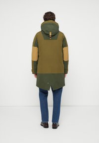 Parka verte avec des accents marron, équipée d'une capuche, de manches longues et d'un ourlet arrondi. Le tissu a une finition texturée et une coupe décontractée.