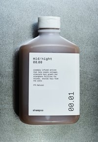 Brun sjampoflaske med matt finish. Hvit etikett med svart tekst som viser ingredienser og fordeler, og skrukork. 97 % naturlig.