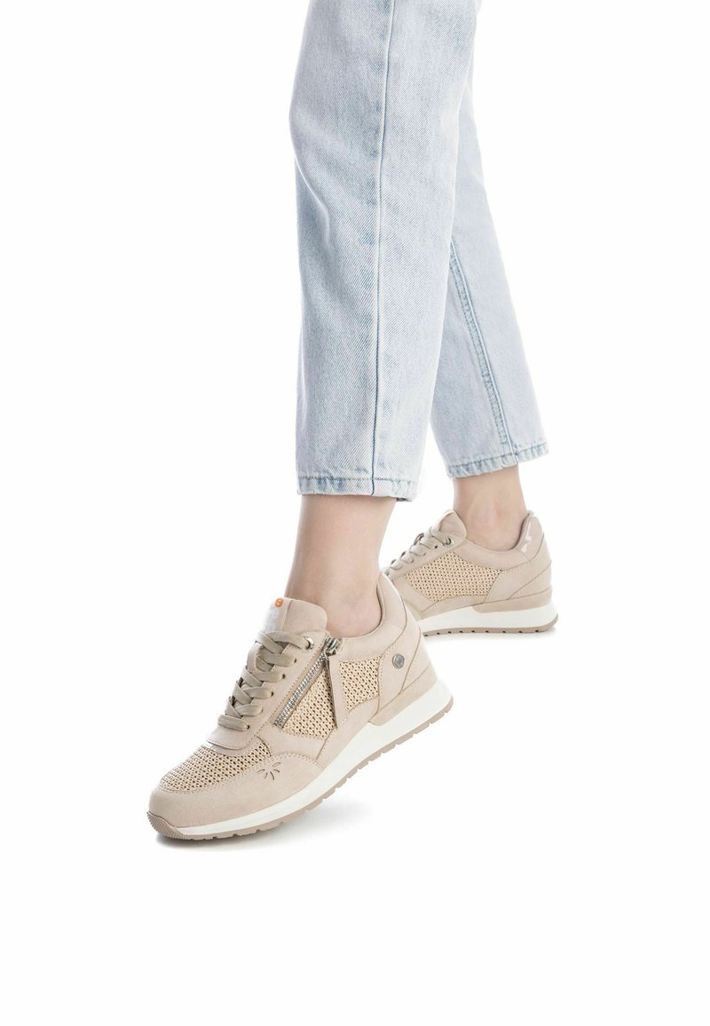 Las zapatillas beiges presentan un diseño de malla y ante, con un zipper lateral y una suela acolchada, combinadas con unos vaqueros cortos de color azul claro.