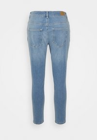 Jeans skinny em denim azul claro com uma cintura de média altura, dois bolsos traseiros e um patch de couro na cintura. Textura suave e forma ajustada.