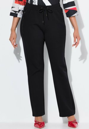 Pantalon de survêtement noir avec une taille à cordon de serrage et des poches zippées sur les côtés. Le tissu est lisse avec une texture légèrement extensible.
