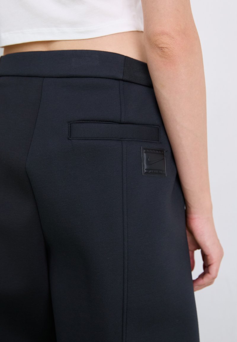 Pantaloni della tuta blu scuro realizzati in tessuto liscio, con una tasca posteriore dotata di una toppa con logo nera e una vita elasticizzata.