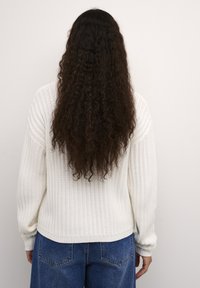 Maglione bianco a coste con maniche lunghe, vestibilità morbida e texture soffice. Abbinato a jeans in denim blu a vita alta.