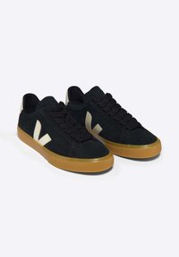 Sneaker in suede nera con suola in gomma color sabbia, caratterizzate da un design con lacci neri e accenti di logo chiari sui lati.