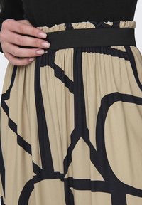 Falda beige con patrones geométricos negros, que cuenta con una cinturilla elástica con volantes y una suave textura de tela que cae.
