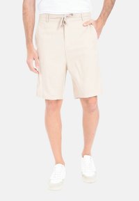 Pantaloni corti beige con vita elasticizzata, design lungo fino al ginocchio, tasche a filo e una texture liscia. Abbinati a sneakers bianche.