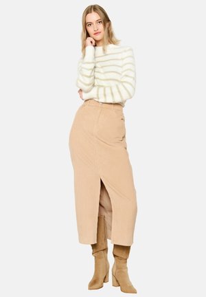 Jupe portefeuille en velours côtelé beige, mi-longue avec une fente frontale. Pull blanc avec de légères rayures horizontales. Bottes beiges jusqu'aux genoux.