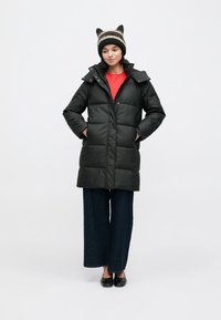 Svart dunjakke med quiltet design, glidelåslukking og sidelommer; kombinert med en rød skjorte og vide, mørke jeans.