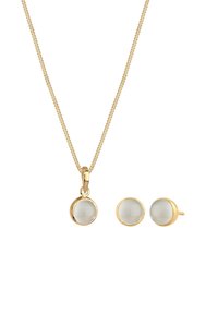 Halskette in Goldton mit rundem Anhänger und passenden runden Ohrsteckern, verziert mit einem glatten, undurchsichtigen weißen Stein.