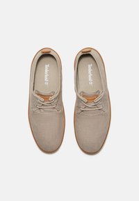 Beiga canvas skor med bruna snöraccenter, rund tå och texturerad gummisula. Timberland-logotyp på innersulan.