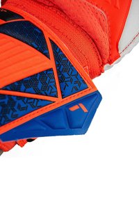 Scarpa sportiva con tomaia arancione brillante, accenti geometrici blu, superficie testurizzata e imbottitura integrata. Costruzione durevole con dettagli a motivo.