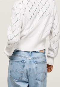 Biały sweter z dzianiny z wzorem w romby i prążkowanym wykończeniem u dołu, zestawiony z jasnoniebieskimi, wysokim stanem dżinsami z tylnymi kieszeniami i przeszyciami.