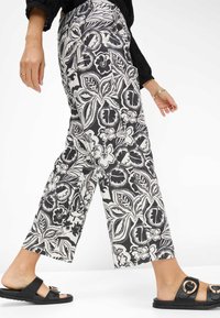 Zwart-witte bloemenpatroon broeken, cropped lengte, lichte stof met een losse pasvorm. Gepaard met zwarte sandalen met gouden accenten.