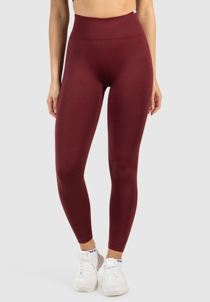 Hooggeknipte bordeaux leggings van een gladde, rekbare stof. Heeft een geribde tailleband en een aansluitend ontwerp, gecombineerd met witte sportschoenen.