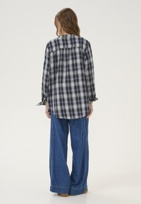 Geverifieerde flanellen overhemd in marineblauw en wit, met een ronde zoom, lange mouwen en een losse pasvorm, gecombineerd met wijde denim broeken.