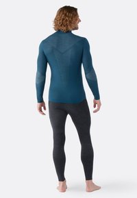 Blauw sportshirt met lange mouwen en een gematteerde achterkant, gecombineerd met grijze aangesloten leggings. De stof lijkt zacht en rekbaar, ontworpen voor actieve inzet.