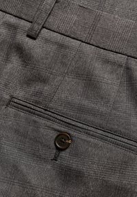 Poche arrière d'un pantalon de costume à carreaux gris avec un bouton marron foncé et un passant de ceinture.