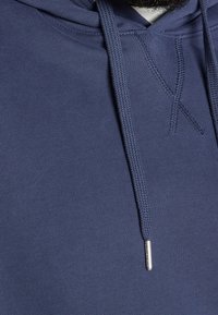 Felpa con cappuccio di colore blu navy, realizzata in un tessuto morbido e testurizzato. Presenta un cappuccio foderato, cordini intrecciati e un dettaglio in metallo per la regolazione.