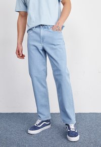 Jeans en denim bleu clair avec une coupe droite, accompagnés de baskets bleu marine avec des accents blancs. Texture lisse, design basique.