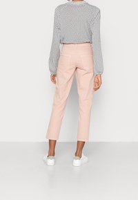 Pantalons roses clairs coupés avec une texture lisse, associés à un haut à pois noir et blanc et des baskets blanches avec des accents gris.
