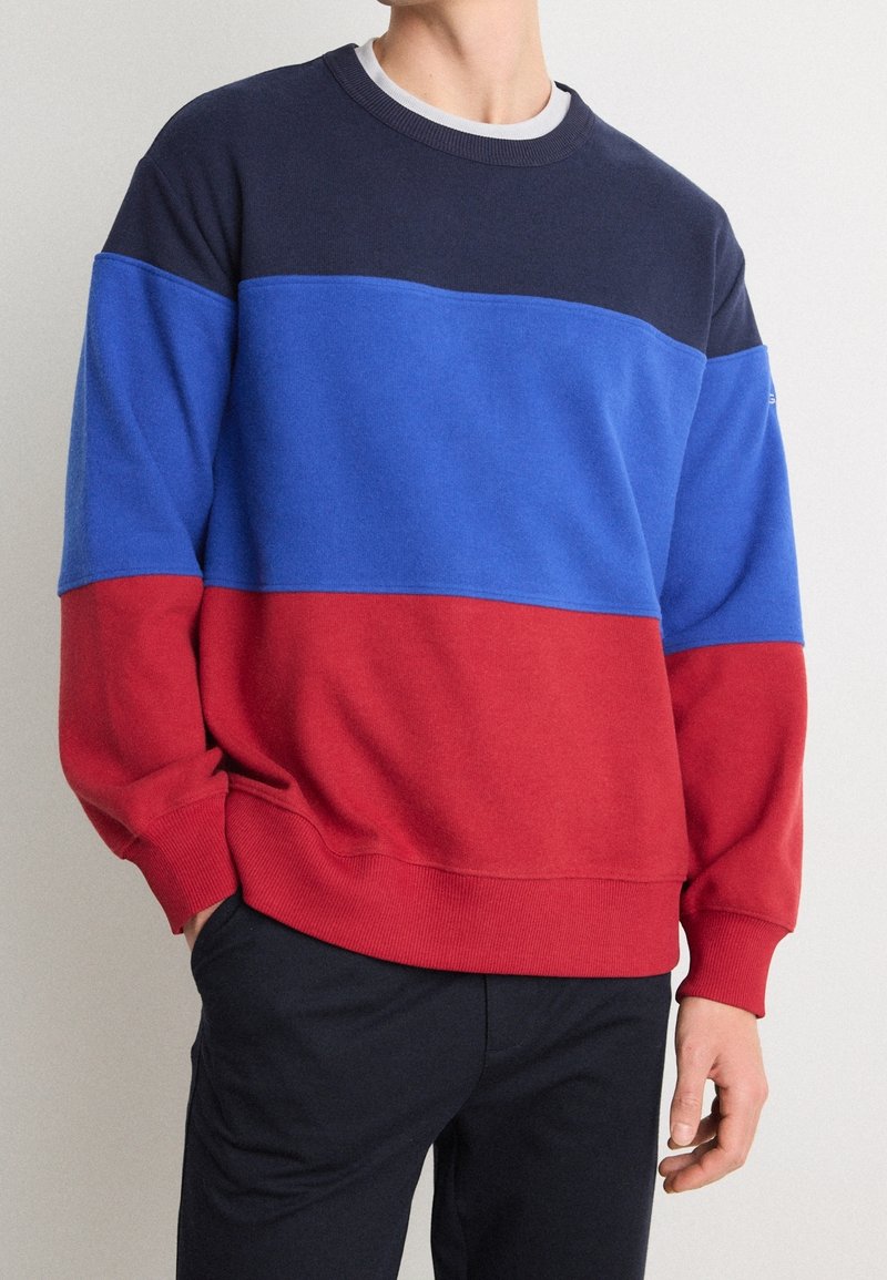Sudadera con bloques de color que presenta secciones en azul marino, azul y rojo. Hecha de algodón con cuello redondo y puños acanalados. Textura suave.
