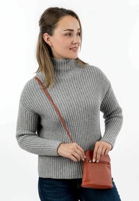 Maglione grigio a costine con un collo alto, abbinato a una piccola borsa a tracolla in pelle rossa con tasca con zip.
