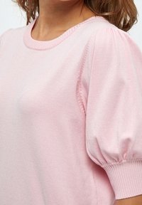 Rosa gestrickter Pullover mit kurzen Puffärmeln, einem runden Ausschnitt und gerippten Bündchen. Der Stoff wirkt weich und hat eine glatte Textur.