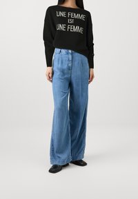 Svart tröja med texten "UNE FEMME EST UNE FEMME", ihopparat med ljusblå vida denimjeans och svarta klackskor.