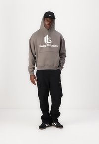 Gray hoodie with "bwlghtsstudios" logo, black cargo pants with pockets, black sneakers with white stripes, and a black cap.