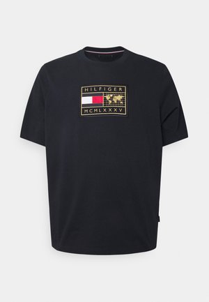 Schwarzes T-Shirt mit kurzen Ärmeln und einem rechteckigen Aufnäher, der eine rot-weiß-blaue Flagge, eine goldene Weltkarte und den Text "HILFIGER MCMLXXXV" zeigt.