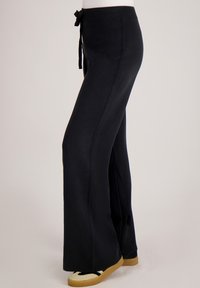 Zwarte wijde broek van zachte stof, met een tailleband met trekkoord en een gladde textuur. Geen zichtbare patronen of hardware.