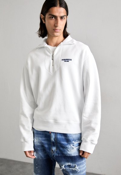 Witte zip-up sweatshirts met een V-vormig ontwerp en een marineblauw logo "DSQUARED2 MILANO." Gecombineerd met versleten blauwe jeans. Zachte textuur, casual pasvorm.
