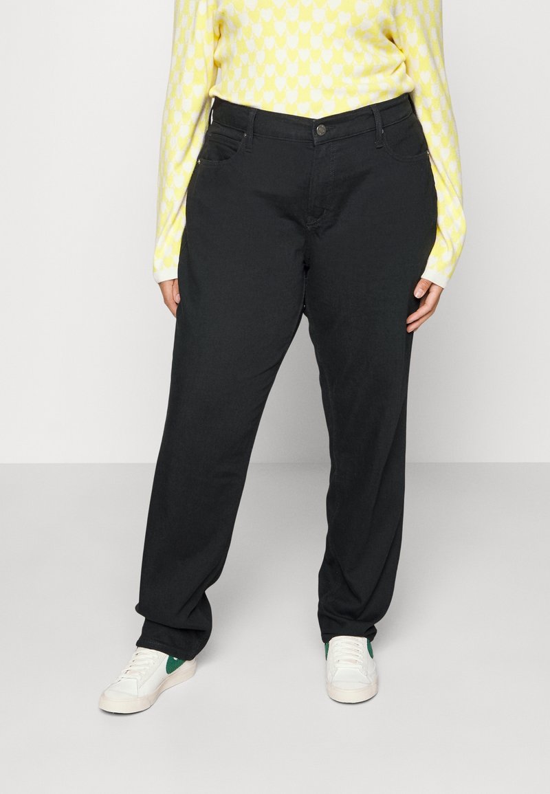Zwarte, loszittende broek met een gladde textuur en voorzakken, gecombineerd met een gele gebreide trui met patroon en witte sportschoenen.